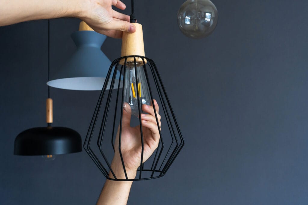 A Hand Changes A Light Bulb In A Stylish Loft Lamp