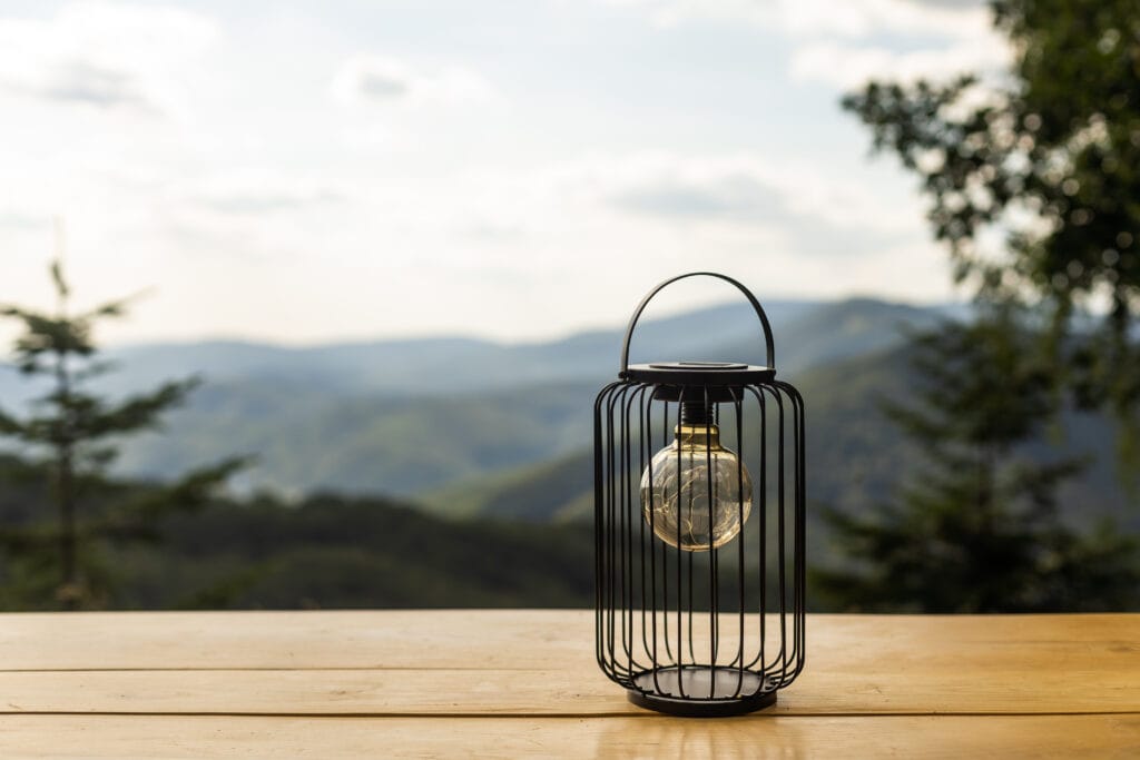 An old lamp lit with the sunset sky and mountains in the background