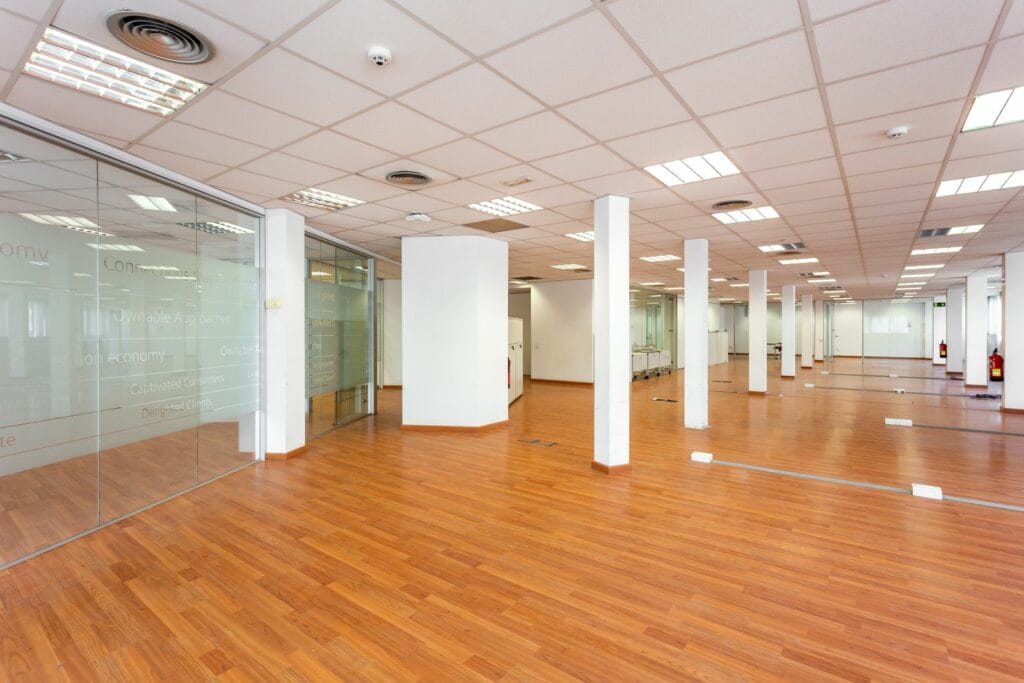 Large Empty Space With Ceiling Tiles, Fluorescent Lights, Light Brown Laminate Flooring And White Painted Columns. Large Office Space For Rent Just Renovated And Unfurnished