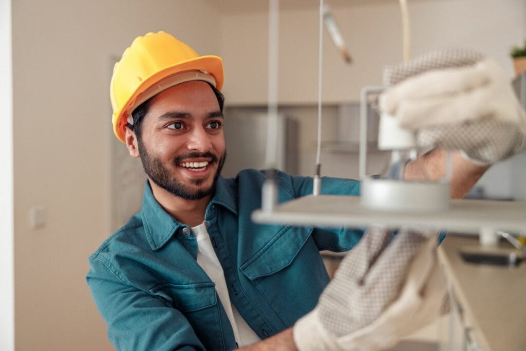 Professional Electrician In Uniform Is Installing The Light Bulbs Into The Chandelier At Home 