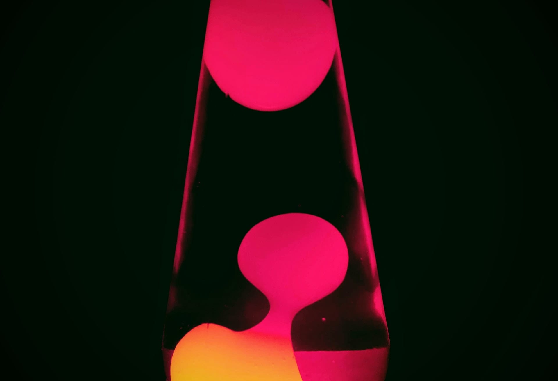 a lava lamp with pink and yellow light on a dark background