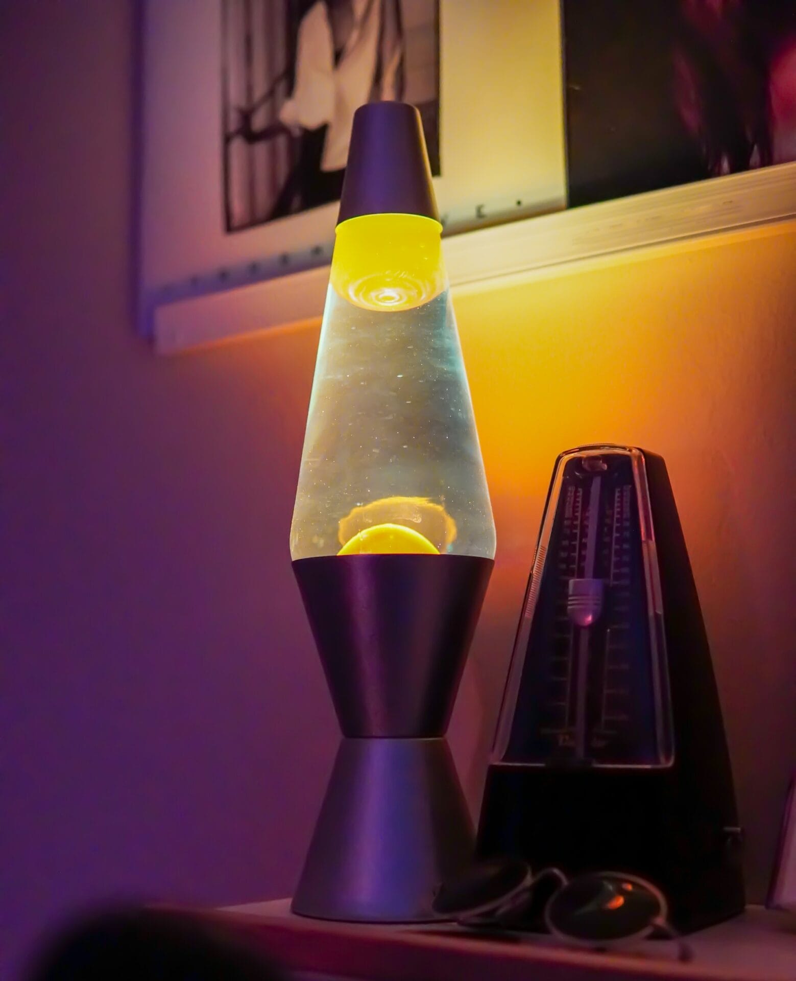 a lava lamp on a desk with eye glass and a wall art in the background