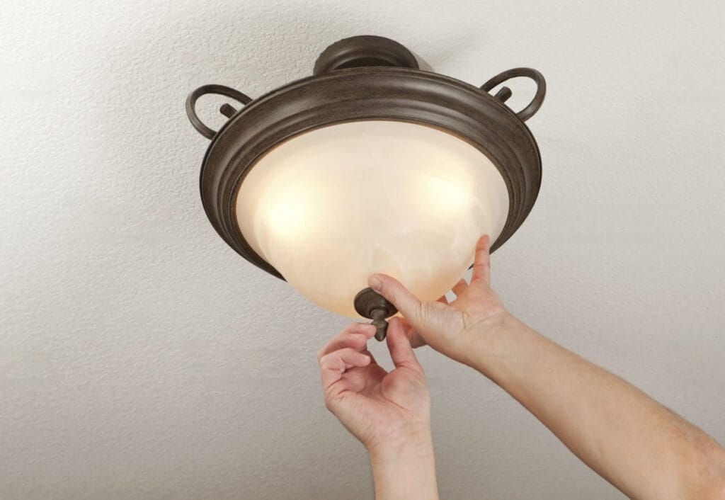 A hand loosening a light fixture cover to replace and clean the fixture.