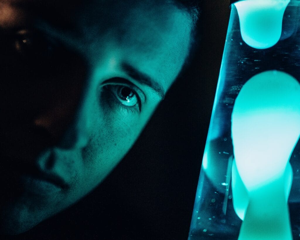 A man deeply staring at a cyand-colored lava lamp.