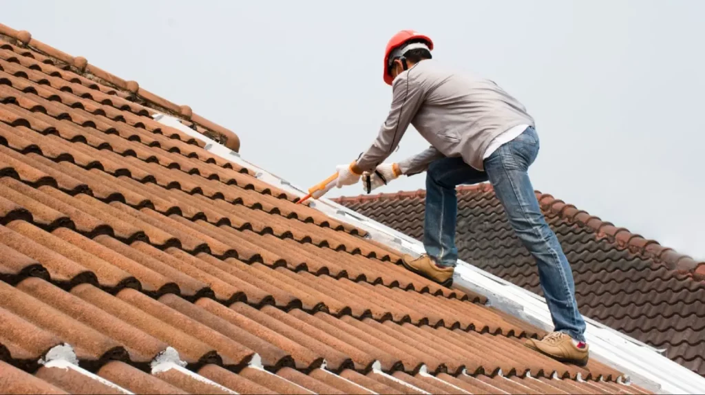 A man appliying silicone caulk on clay tile roof.